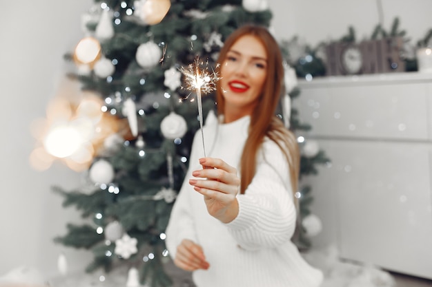 Donna in un maglione bianco seduto vicino all'albero di natale