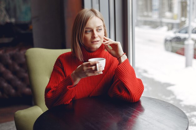 Donna in un maglione rosso. La signora beve un caffè.