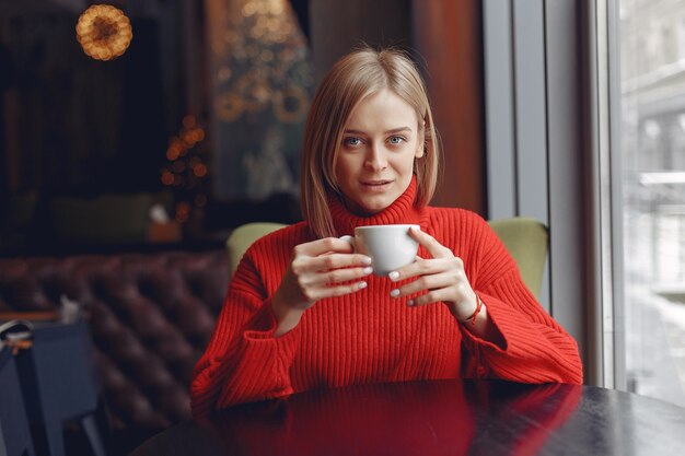 Donna in un maglione rosso. La signora beve un caffè.