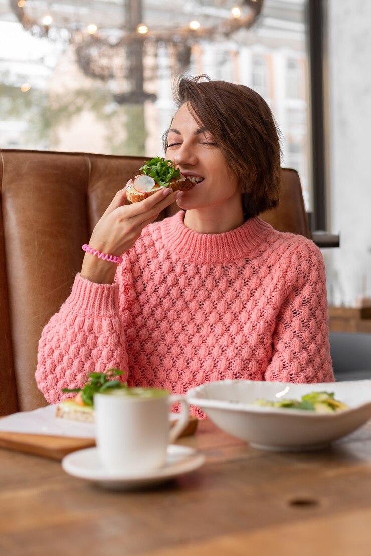 Foto gratuito donna in un ristorante con un accogliente maglione caldo che mangia un toast sano per la colazione con arugula e salmone