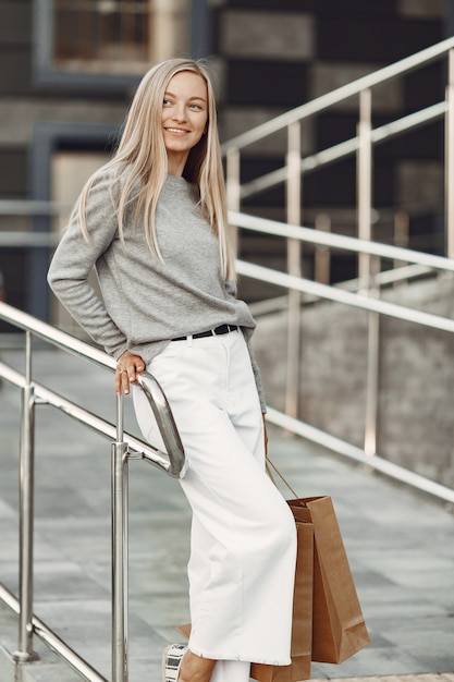 Donna in una città estiva. Signora con borse marroni. Donna in un maglione grigio.