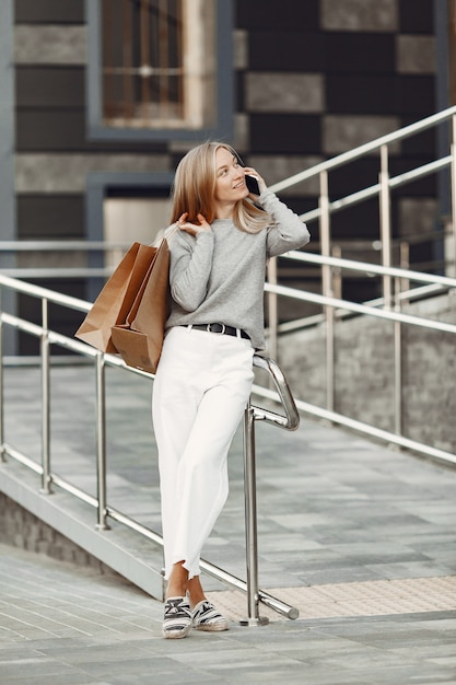 Donna in una città estiva. Signora con il cellulare. Donna in un maglione grigio.