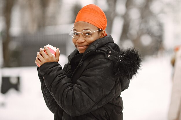 Donna in una città invernale. Ragazza in una giacca nera. Donna africana con caffè.