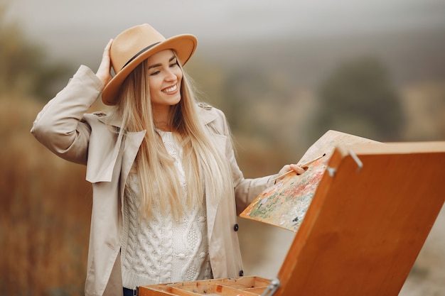 Donna in una pittura del cappotto marrone in un campo