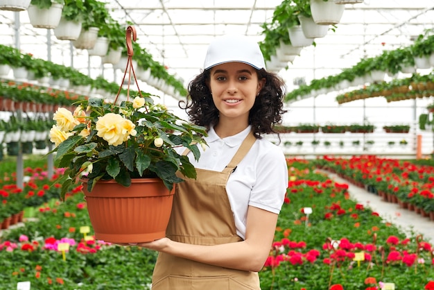 Donna in uniforme in posa in serra con vaso di fiori