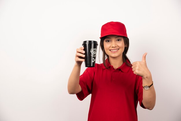 Donna in uniforme rossa che mostra una tazza di caffè su priorità bassa bianca.