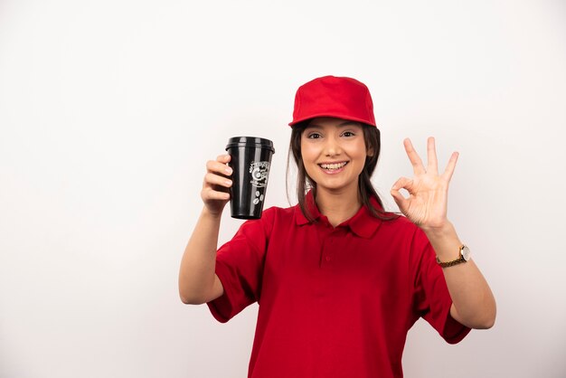 Donna in uniforme rossa che mostra una tazza di caffè su priorità bassa bianca.