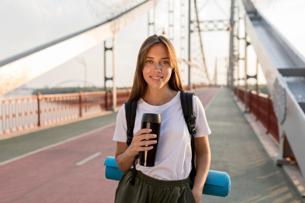 Donna in viaggio in posa sul ponte con thermos e zaino