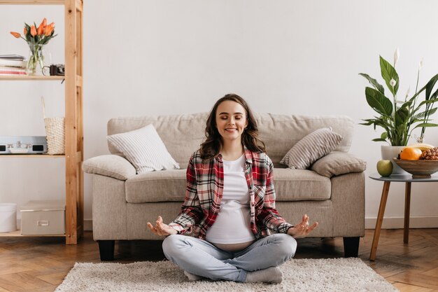 Donna incinta allegra di buon umore meditando sul tappeto morbido beige