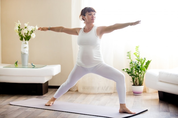 Donna incinta che fa guerriero Due posa di yoga a casa