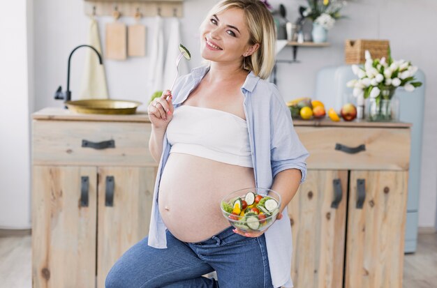 Donna incinta che mangia insalata mentre esaminando la macchina fotografica