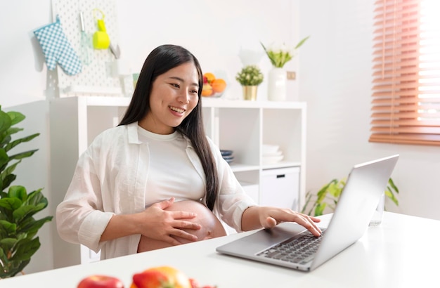 Donna incinta che per mezzo del computer portatile a casa