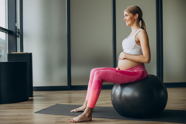 Donna incinta che si esercita con fit ball su una classe di pilates