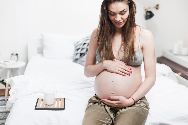 Donna incinta che si siede sul letto che tocca la sua pancia