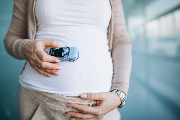 Donna incinta che tiene piccolo modello di automobile dalla pancia