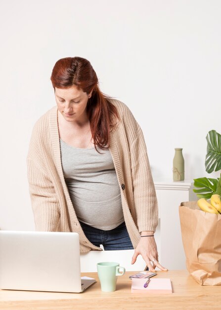 Donna incinta dell'angolo alto che esamina computer portatile