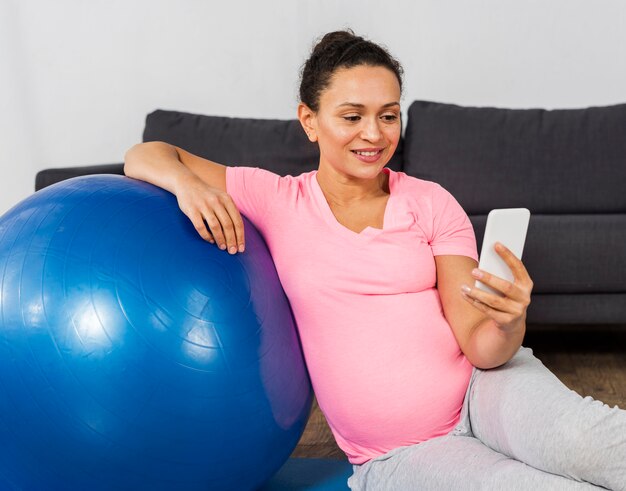 Donna incinta di smiley che utilizza smartphone durante l'allenamento a casa