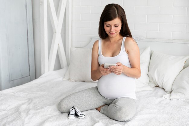 Donna incinta di vista frontale che controlla il suo telefono