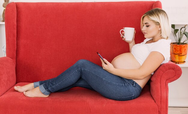 Donna incinta di vista laterale che osserva sul suo telefono