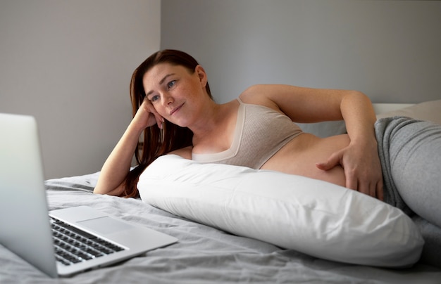 Donna incinta di vista laterale con il computer portatile a casa