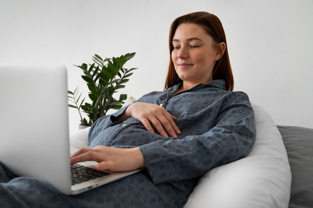 Donna incinta di vista laterale con il computer portatile a casa