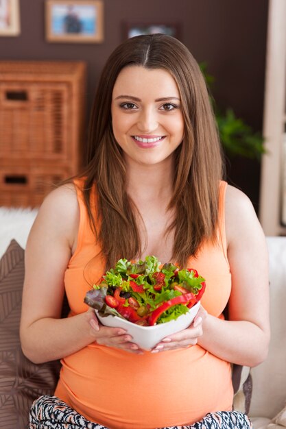 Donna incinta felice che mangia insalata sana