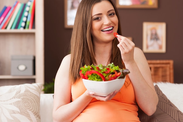 Donna incinta felice che mangia insalata sana