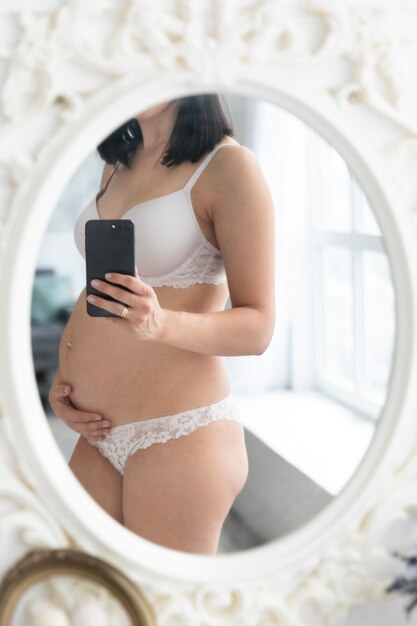 Donna incinta in biancheria intima che prende una foto
