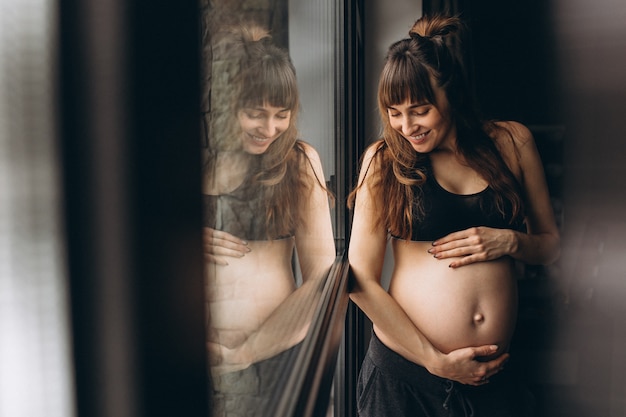 Donna incinta in piedi vicino alla finestra