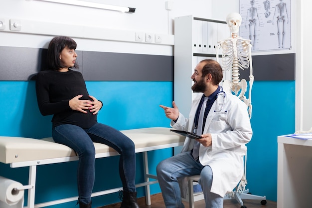 Donna incinta incontro con il medico all'appuntamento di controllo. Medico che consulta il paziente in attesa del bambino, fornisce supporto e controlla l'assistenza sanitaria in studio medico. Esame di gravidanza