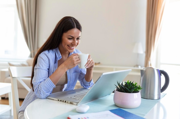 Donna indipendente che lavora con il suo computer portatile a casa con una tazza di caffè