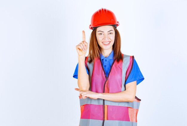 Donna ingegnere in uniforme e casco rosso che mostra qualcosa.