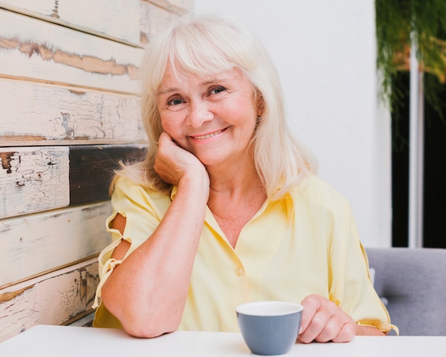 Donna invecchiata che si siede nella cucina con sorridere della tazza