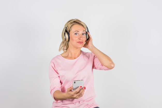 Donna invecchiata in camicia rosa con le cuffie tramite smartphone