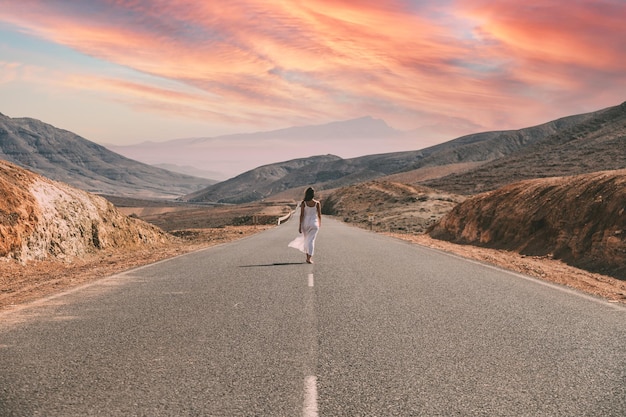 Donna irriconoscibile che cammina sulla strada vicino alle colline sotto il cielo nuvoloso