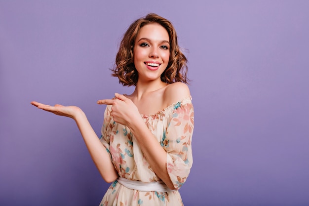 Donna ispirata con capelli ricci castani in posa con piacere in camera con interni viola