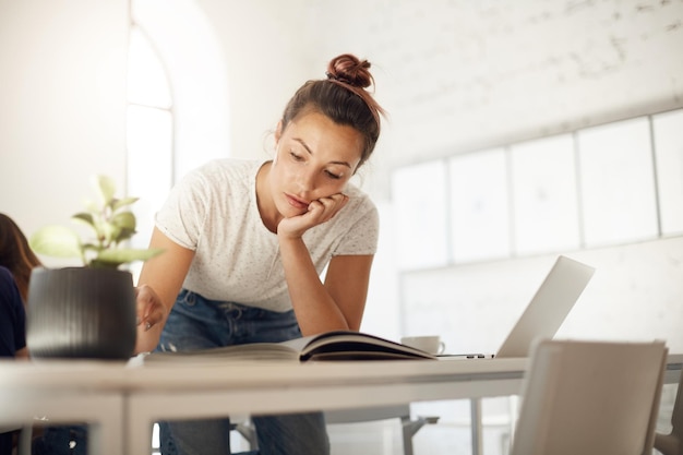 Donna laboriosa che lavora alla sua collezione di stilisti guardando attraverso una rivista di moda per trovare ispirazione