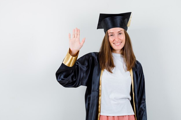 Donna laureata agitando la mano per il saluto in abiti casual, uniforme e gioiosa. vista frontale.