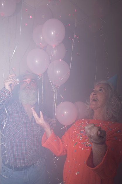 Donna maggiore che esamina suo marito che soffia bolle di sapone in festa di compleanno