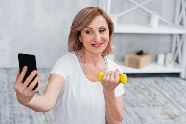 Donna maggiore che prende selfie con i dumbbells a disposizione