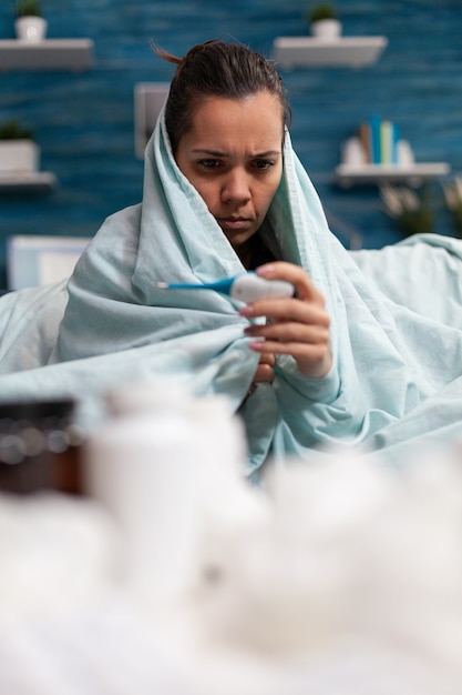 Donna malata che misura la temperatura con il termometro a casa che si sente male adulto che controlla febbre e virus