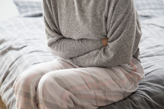 Donna malata sul letto tenendo le mani sullo stomaco, soffre di dolore