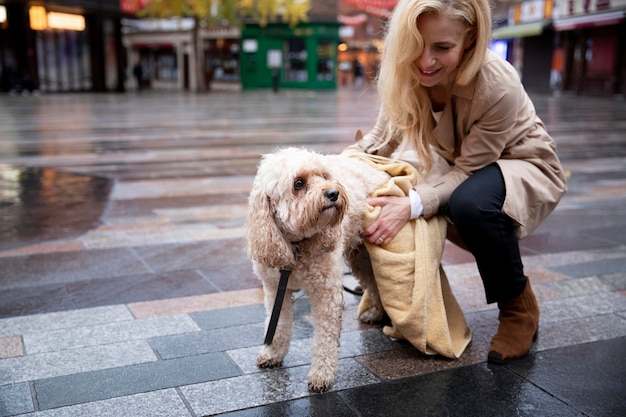 Donna matura che asciuga il suo cane durante la passeggiata mentre piove