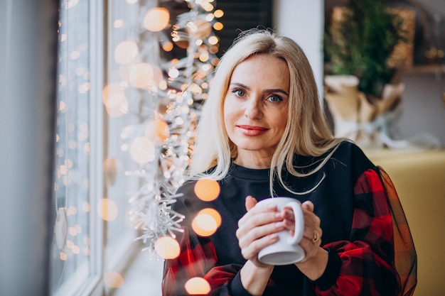 Donna matura che beve il caffè vicino alla finestra