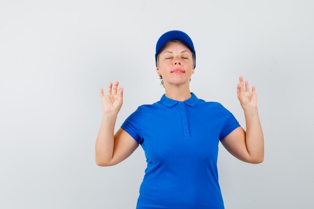 Donna matura che fa meditazione con gli occhi chiusi in maglietta blu e che sembra pacifica