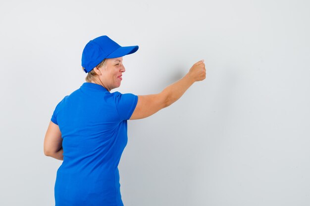 Donna matura che finge di bussare alla porta in maglietta blu e sembra eccitata, vista posteriore.