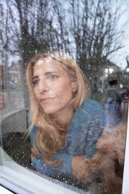 Donna matura che guarda fuori dalla sua finestra mentre piove