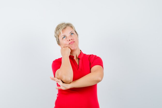 Donna matura che sostiene il mento sul pugno in maglietta rossa e che sembra pensieroso