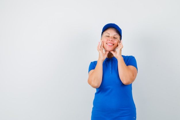 Donna matura che tocca la sua pelle del viso in maglietta blu e sembra carina