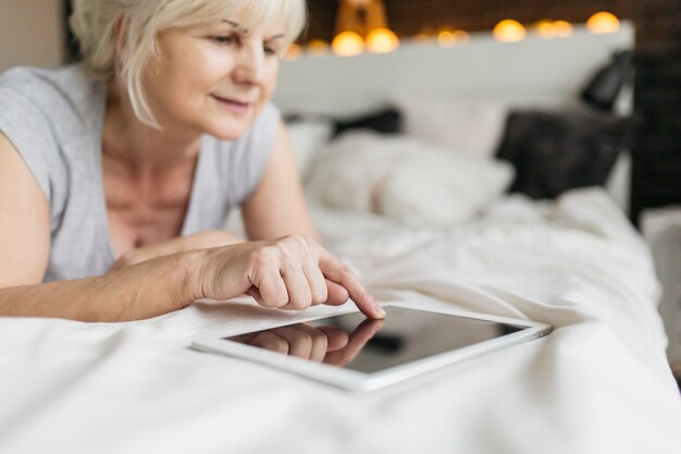 Donna matura che utilizza compressa nella camera da letto